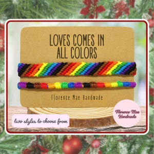 May include: Two woven bracelets displayed on a rectangular tan card with the text LOVES COMES IN ALL COLORS and Florence Mae Handmade. The top bracelet features a diagonal rainbow stripe pattern, while the bottom bracelet has a knotted design.
