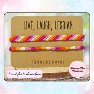 May include: Two friendship bracelets with the text "LIVE, LAUGH, LESBIAN" and "Florence Mae Handmade". The bracelets are made with pink, orange, and white string.