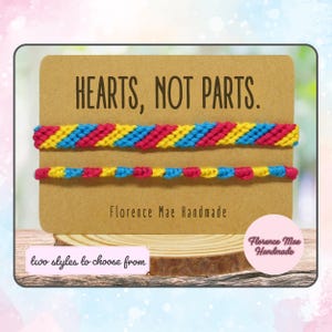 May include: Two friendship bracelets with the text "HEARTS, NOT PARTS."  The bracelets are made with blue, yellow, and pink string. The bracelets are displayed on a brown card with the text "Florence Mae Handmade".