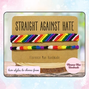 May include: Two friendship bracelets with the words "Straight Against Hate" and "Florence Mae Handmade" on a brown card. The bracelets are made with rainbow colored string and black string. The bracelets are in two different styles, one with a diagonal pattern and one with a straight pattern.
