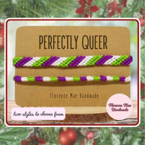 May include: Two woven bracelets featuring purple, lime green, and white diagonal stripes, displayed on a rectangular kraft paper card. The card features the text "PERFECTLY QUEER" and "Florence Mae Handmade" with a "two styles to choose from" label.
