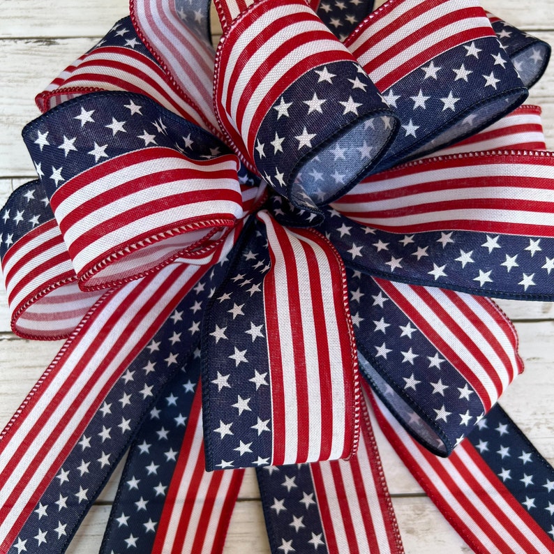 May include: A red, white, and blue bow made from fabric with a stars and stripes pattern. The bow is tied with a loop and tails.