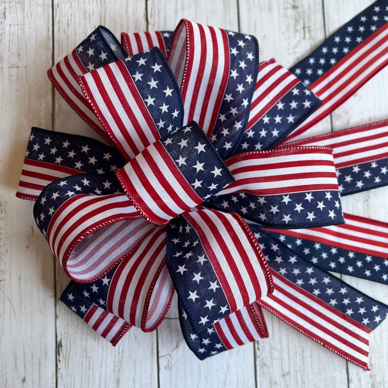 May include: A red, white, and blue American flag bow. The bow is made of fabric and has a star pattern on one side and stripes on the other.