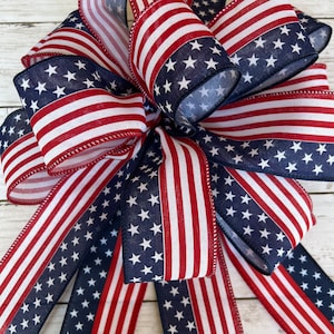May include: A red, white, and blue bow made from fabric with a stars and stripes pattern. The bow is tied with a loop and tails.