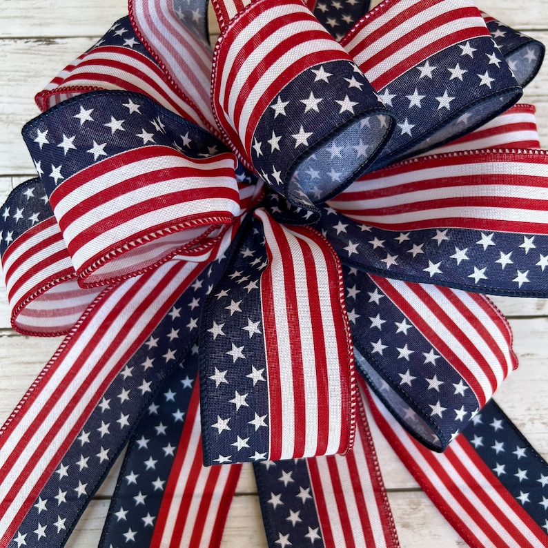 May include: A red, white, and blue bow made from fabric with a stars and stripes pattern. The bow is tied with a loop and tails.