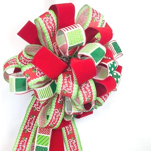 May include: A large Christmas bow with red velvet and patterned ribbons. The ribbons feature the text "Merry Christmas" and green and white designs. The bow is a festive decoration for the holiday season.