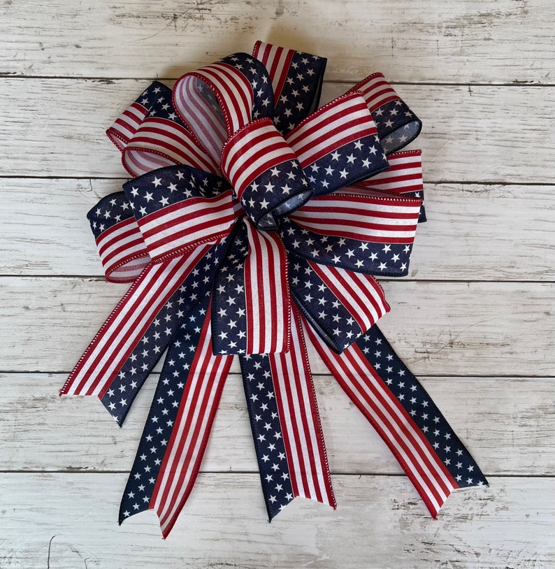 May include: A large red, white, and blue bow made of ribbon with a stars and stripes pattern. The bow is tied in a knot and has multiple tails.