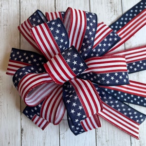 May include: A red, white, and blue American flag bow. The bow is made of fabric and has a star pattern on one side and stripes on the other.