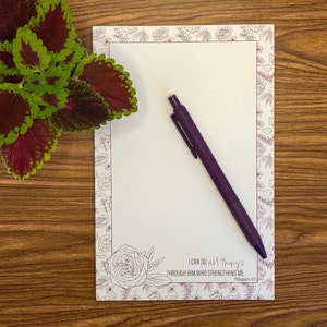 May include: A white notepad with a floral border and a purple pen. The notepad has the text "I can do all things through him who strengthens me" and "Philippians 4:13".