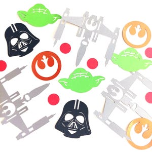 May include: Assorted Star Wars themed paper cutouts, including Darth Vader, Yoda, X-wing fighters, and Rebel Alliance symbols. The cutouts are in black, silver, green, orange, and red. Perfect for themed parties or crafts.