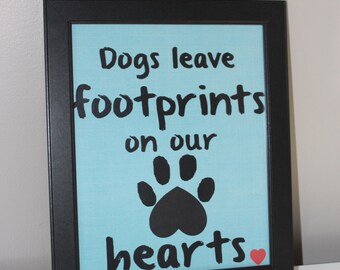 May include: Black framed canvas with a light blue background and the text "Dogs leave footprints on our hearts" in black with a black paw print and a red heart.