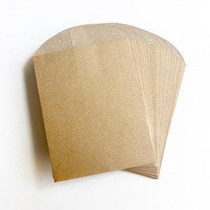 May include: A stack of small, rectangular, light brown kraft paper envelopes with rounded flaps. The text 'Mini Kraft Sack / Envelopes' is printed in green above the stack. The envelopes are plain, unadorned, and have a smooth, matte texture.