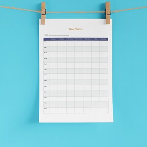 May include: A white study planner sheet with a grid layout, suspended by wooden pegs on a string against a light blue background. The planner includes the title "Study Planner" and a schedule grid for the week.