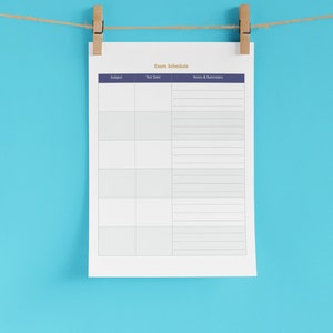 Op de afbeelding: Een printbare examenschema-sjabloon met kolommen voor vak, datum van het examen en notities en herinneringen. De sjabloon staat op een wit vel papier met een blauwe kop en hangt aan een touwtje met wasknijpers.