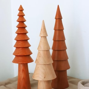 May include: Three wooden Christmas tree ornaments in different sizes. The largest tree is a deep orange color, the middle tree is a light brown color, and the smallest tree is a light brown color. The trees are all made of wood and have a smooth finish.