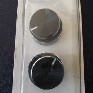 May include: Two black round knobs with a silver trim. The knobs are packaged in a clear plastic blister pack.