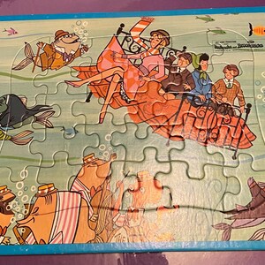 May include: A vintage jigsaw puzzle featuring a cartoon illustration of a group of people on a bed floating in the ocean. The puzzle is set against a blue background with white puzzle pieces. The text "Walt Disney's Wonderful World of Color" is printed on the puzzle.