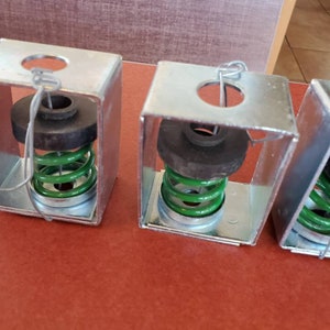 May include: Three silver metal boxes with a green spring inside each box. The boxes have a round hole in the top and a small metal hook attached to the top.