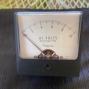 May include: A black and silver analog AC voltmeter with a white face and a needle pointing to the 4 volt mark. The meter reads "AC VOLTS RECTIFIER TYPE Simpson 2000 Ω/V".