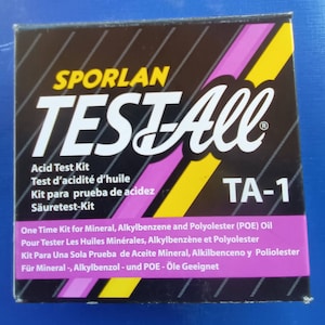 May include: A black box with yellow and pink stripes. The box has white text that reads "SPORLAN TESTAll" and "TA-1". The box is labeled as an "Acid Test Kit" for mineral, alkylbenzene, and polyolester oil.