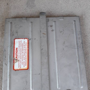 May include: A silver metal battery cover with a red warning label that reads "CAUTION MAINTAIN ONLY IN ACCORDANCE WITH SAFT MAINTENANCE MANUAL. USE DISTILLED OR DEIONIZED WATER. ANY TRACE OF ACID WILL PERMANENTLY DESTROY CELLS."