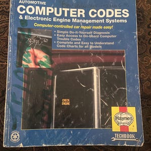 May include: A blue Haynes Techbook manual titled Automotive Computer Codes & Electronic Engine Management Systems, number 10205. The cover features a car dashboard with a Check Engine light and a small inset photo of a hand using a diagnostic tool.