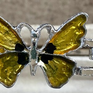 May include: A silver-toned bracelet featuring a butterfly design. The butterfly has yellow wings with black accents. The bracelet is made of metal and has a simple, elegant design.