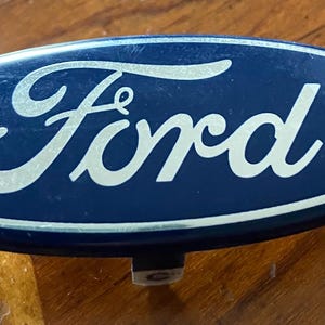 May include: A blue oval car emblem with a silver Ford logo.