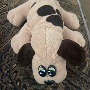 May include: A brown and black plush dog toy with large black eyes. The dog has brown spots on its back.