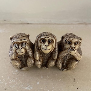 May include: A figurine depicting the Three Wise Monkeys: See no evil, hear no evil, speak no evil. The monkeys are in a row, each with a different pose. The monkeys are beige with brown details.