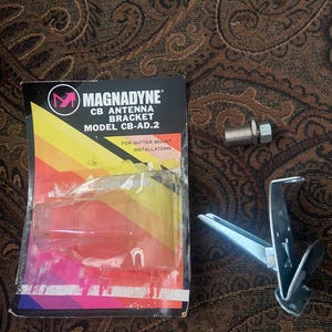 May include: A Magnadyne CB antenna bracket, model CB-AD.2, with a metal mounting clip and hardware. The bracket is packaged in a colorful box with the text "For Gutter Mount Installations."