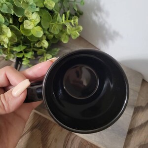 Op de afbeelding: Een zwarte keramische koffiemok met een gladde, glanzende afwerking. De mok is leeg en de binnenkant is zichtbaar.