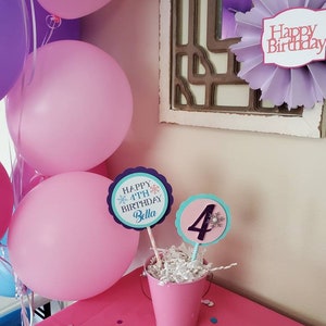 May include: A pink birthday party scene with balloons, decorations, and a table. The table has a pink tablecloth and a small pink bucket with birthday signs that read "Happy 4th Birthday Bella" and the number "4".