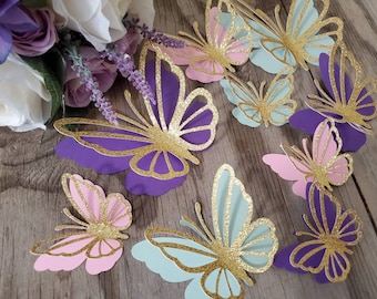 May include: A collection of 10 paper butterflies with gold glitter accents. The butterflies are in shades of purple, pink, and blue.
