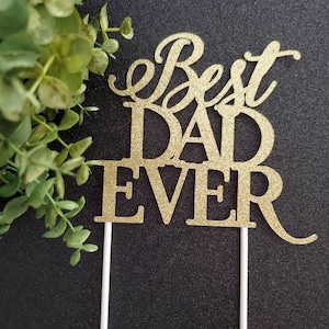 May include: Gold glitter cake topper with the words "Best Dad Ever" on it. The topper is on two white sticks.