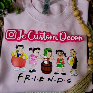 May include: Pink sweatshirt with a graphic of cartoon characters and the text "Friends" in black. The text "Jc Custom Decon" is in white letters on a pink background.