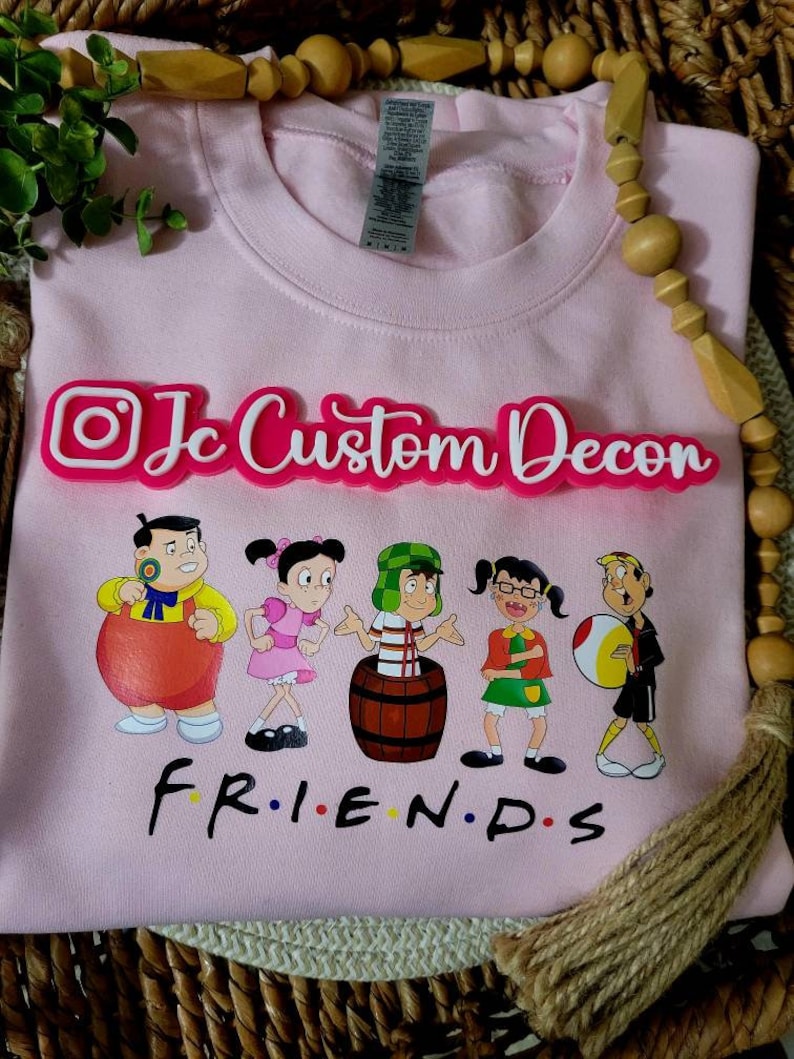 May include: Pink sweatshirt with a graphic of cartoon characters and the text "Friends" in black. The text "Jc Custom Decon" is in white letters on a pink background.