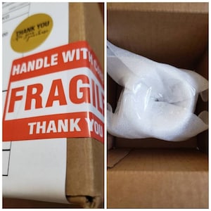 Op de afbeelding: Een bruine kartonnen doos met een rood-witte "HANDLE WITH CARE FRAGILE" sticker en de tekst "THANK YOU" erop gedrukt. De doos is gevuld met witte verpakkingsnoepjes.