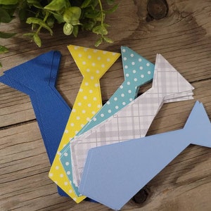 May include: Four paper tie shapes in blue, yellow, light blue, and gray with white polka dots and plaid patterns.