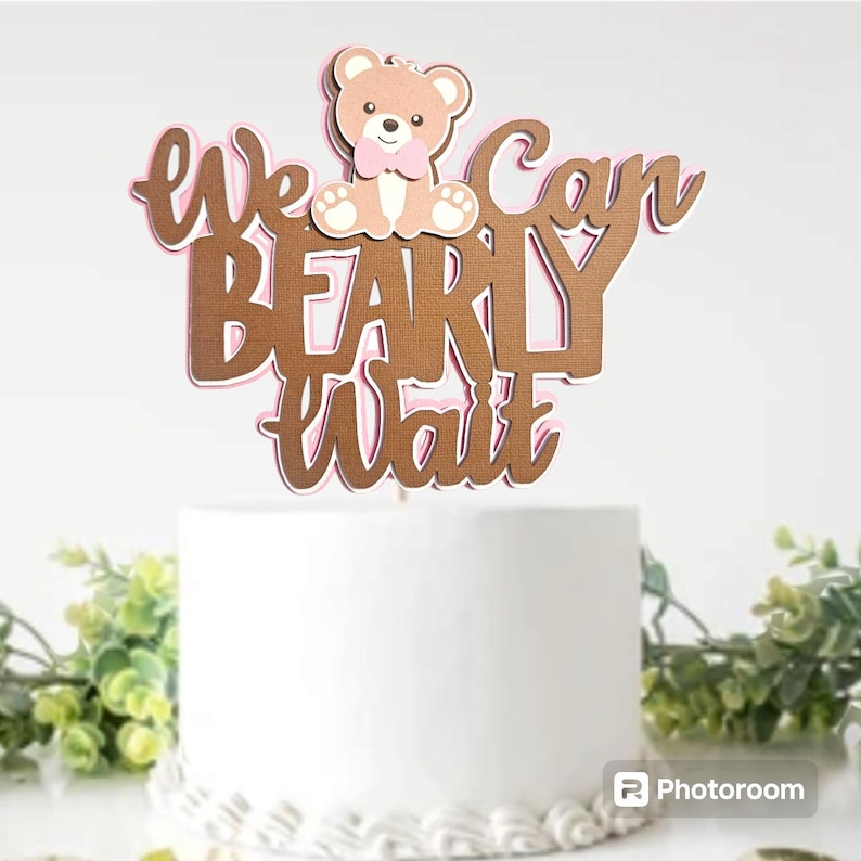 May include: A brown and pink cake topper with a teddy bear and the text "We can barely wait".