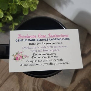 Op de afbeelding: Een witte kaart met zwarte tekst en roze accenten geeft onderhoudsinstructies voor drinkwaren. De kaart luidt "Drinkware Care Instructions Gentle Care Equals Lasting Care Bedankt voor uw aankoop! Drinkware is gemaakt van permanent vinyl en met de hand aangebracht -Niet in de magnetron gebruiken -Niet in water weken -Vinyl is niet vaatwasmachinebestendig -Alleen met de hand wassen (decalgebied vermijden)"