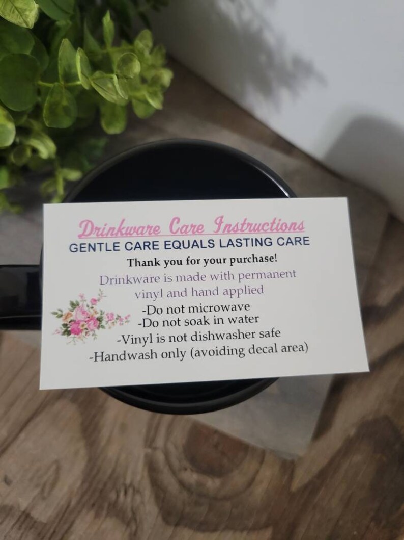 Op de afbeelding: Een witte kaart met zwarte tekst en roze accenten geeft onderhoudsinstructies voor drinkwaren. De kaart luidt "Drinkware Care Instructions Gentle Care Equals Lasting Care Bedankt voor uw aankoop! Drinkware is gemaakt van permanent vinyl en met de hand aangebracht -Niet in de magnetron gebruiken -Niet in water weken -Vinyl is niet vaatwasmachinebestendig -Alleen met de hand wassen (decalgebied vermijden)"