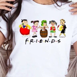 May include: White t-shirt with a cartoon illustration of six friends. The characters are wearing colorful clothing and holding various objects. The text "FRIENDS" is printed below the characters.