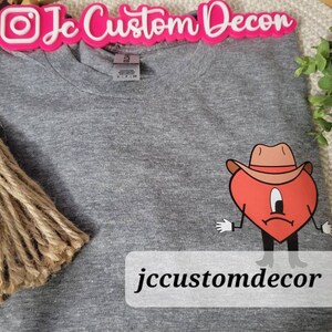 May include: Gray t-shirt with a red heart wearing a cowboy hat and the text "jccustomdecor" printed on the bottom.