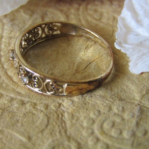 May include: A gold filigree ring with small clear stones set in the band.