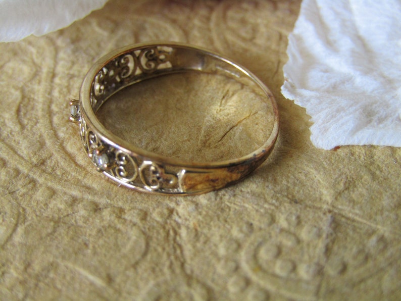 May include: A gold filigree ring with small clear stones set in the band.