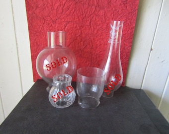 May include: Four clear glass lamp chimneys of varying sizes and shapes. The chimneys are all sold.