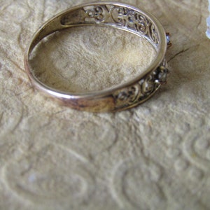 May include: A silver filigree ring with two small clear stones set in the band.