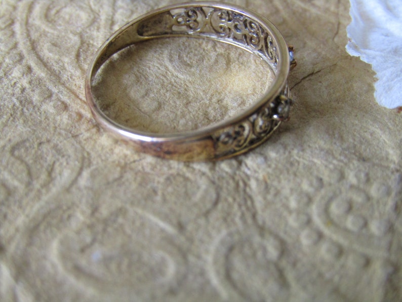 May include: A silver filigree ring with two small clear stones set in the band.