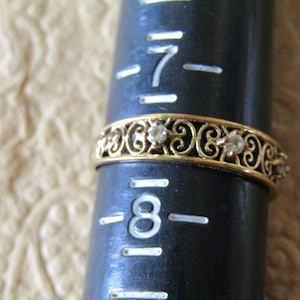 May include: A gold band ring with a delicate filigree design and small clear stones. The ring is sized for a size 8 finger.